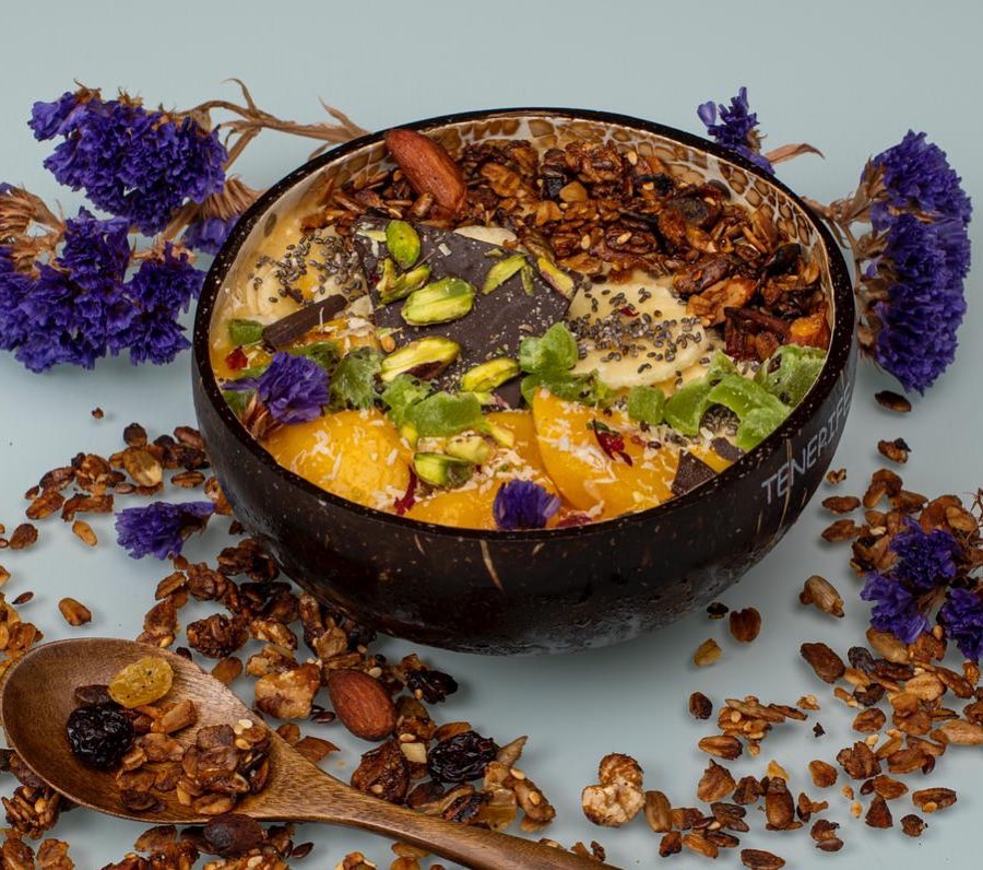 Smoothie bowl con granola, mango, pistachos y flores comestibles