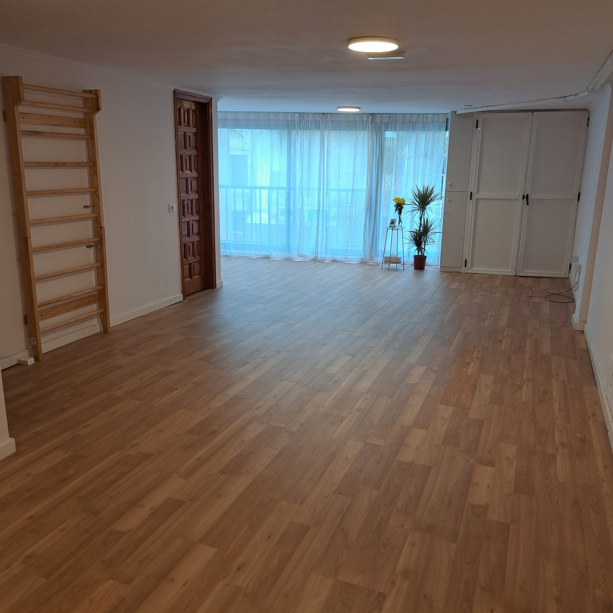 Sala amplia de Ocean and Om con suelo de madera, luz natural, plantas y espaldera de madera