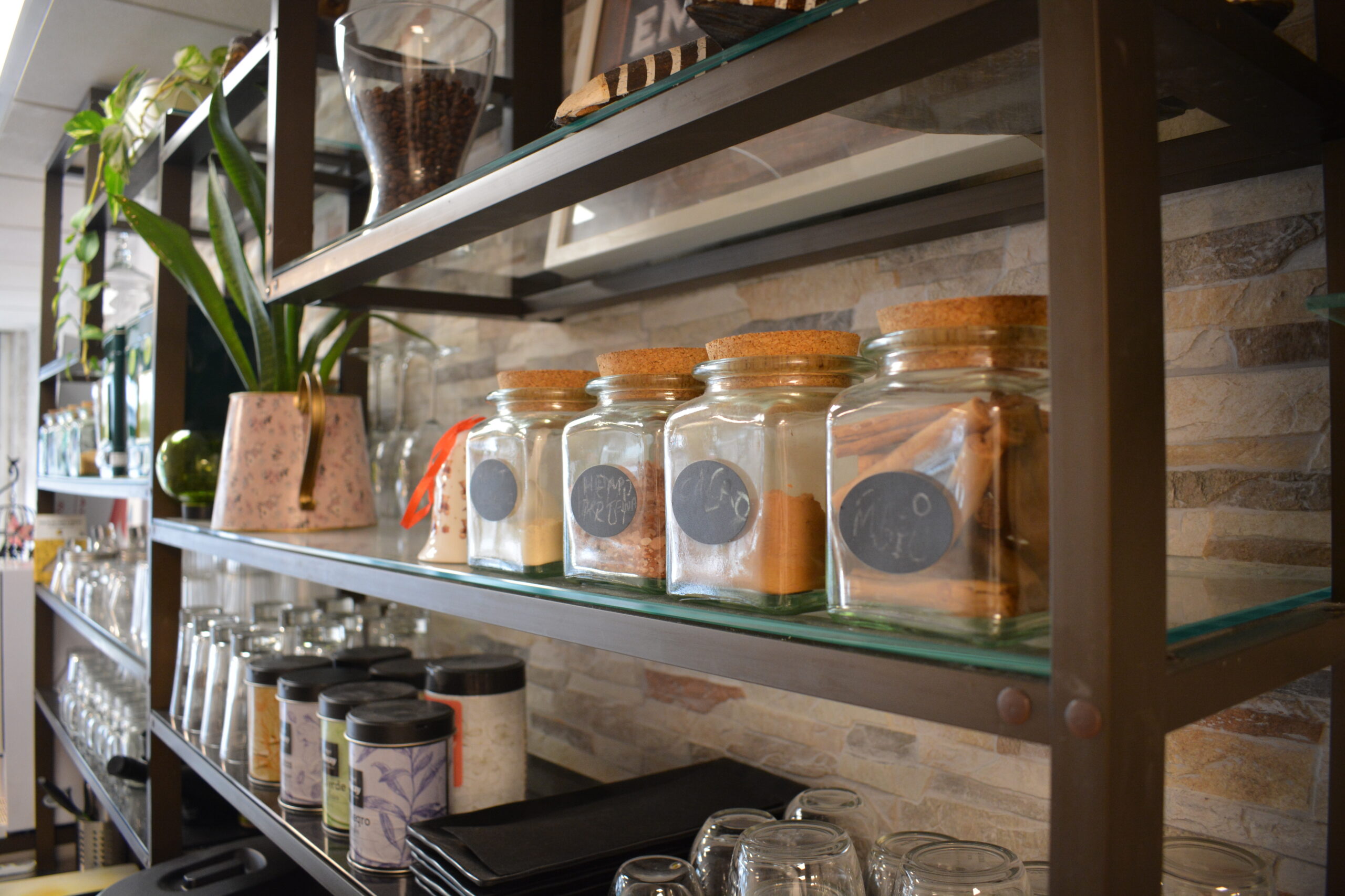 Botes de especias, plantas y vasos en la cocina-café de Ocean and Om