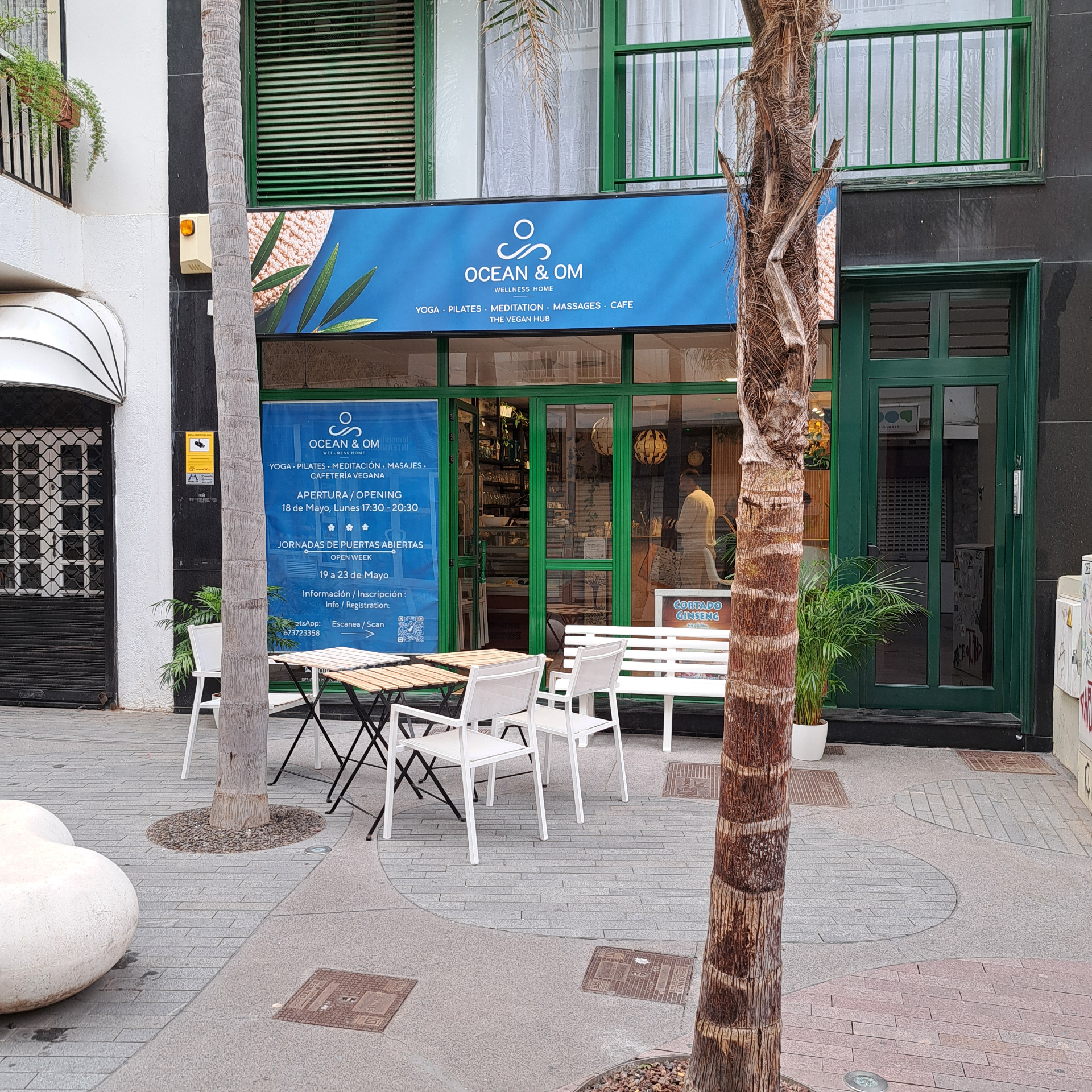 Ocean and Om con mesas exteriores en una calle peatonal con palmeras.