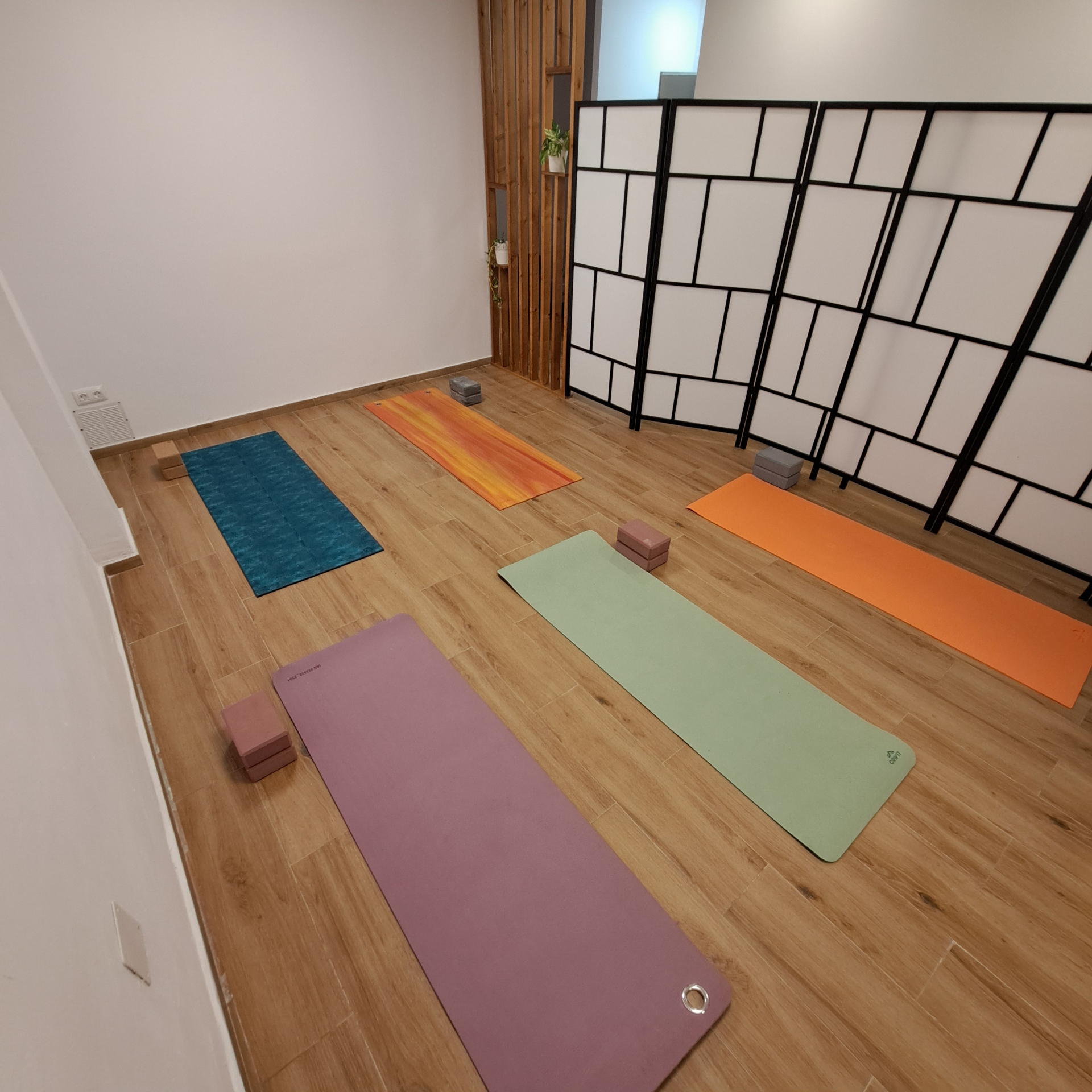 Sala de yoga con esterillas, bloques y paneles divisores decorativos.