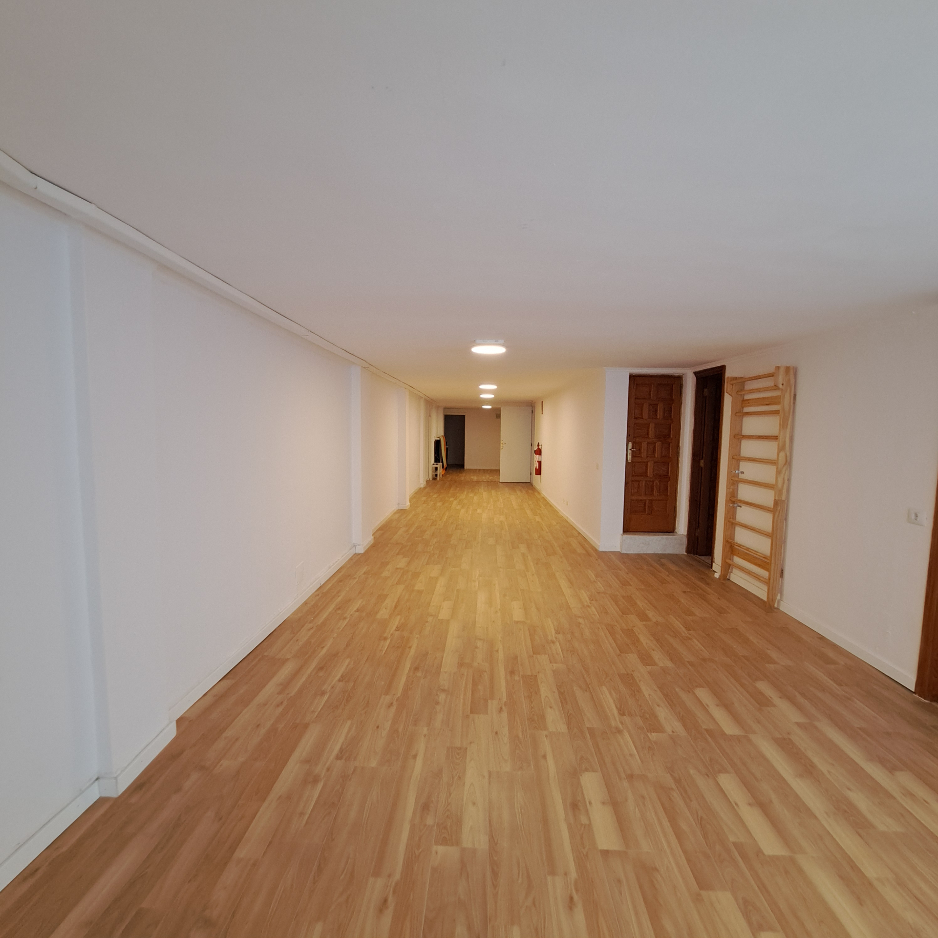 Sala amplia y vacia con suelo claro y luz de techo.