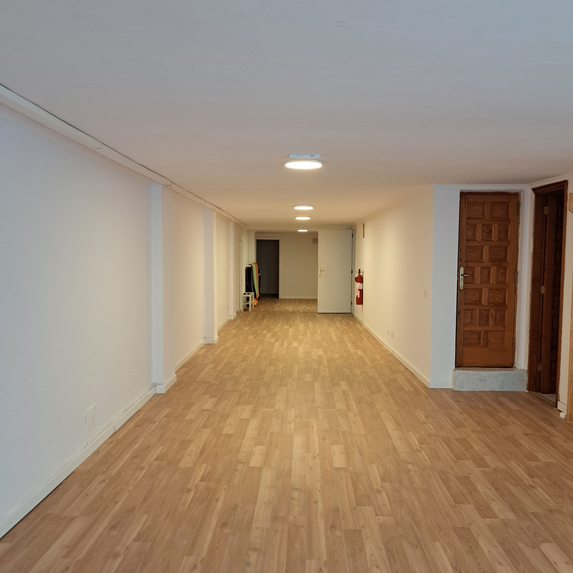 Sala amplia vacia con suelo de madera, paredes blancas y puertas.