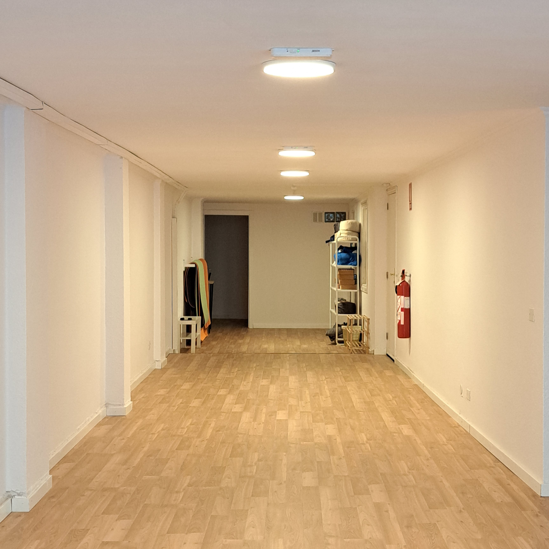 Sala vacia con estanterias, sillas apiladas y puerta al fondo.
