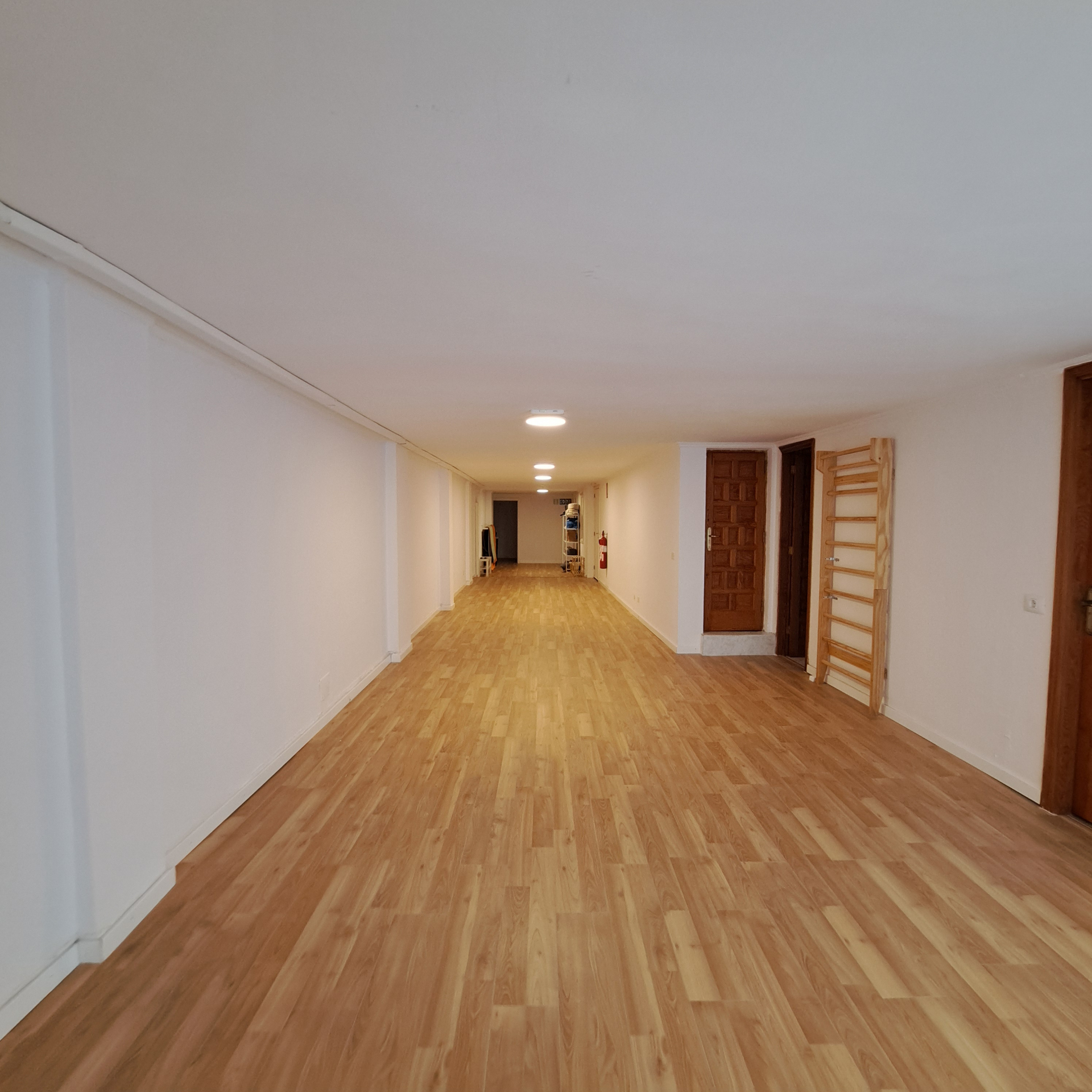 Pasillo interior del centro con suelo de madera, paredes blancas y varias puertas.