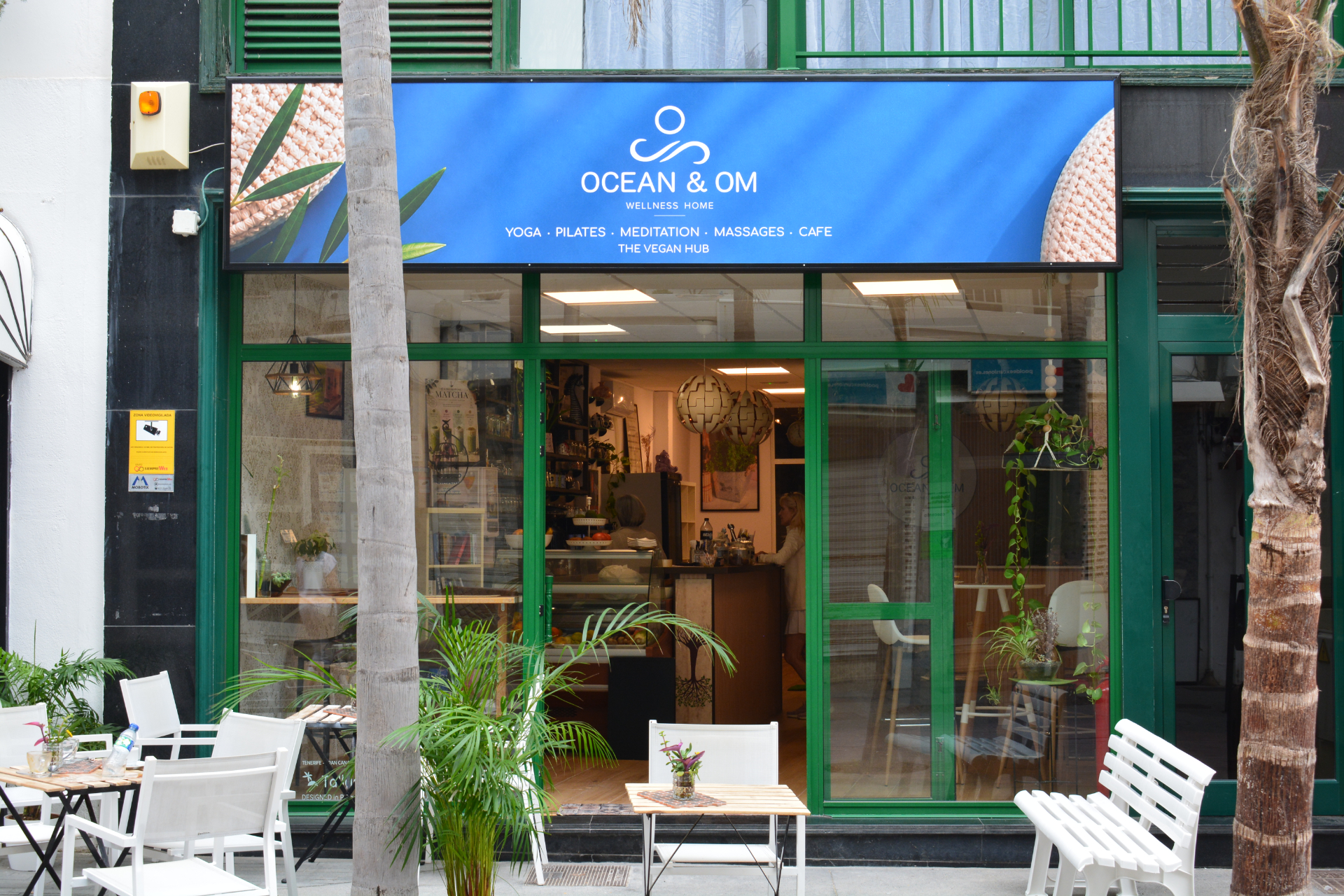Fachada de Ocean and Om con mesas blancas exteriores y plantas.