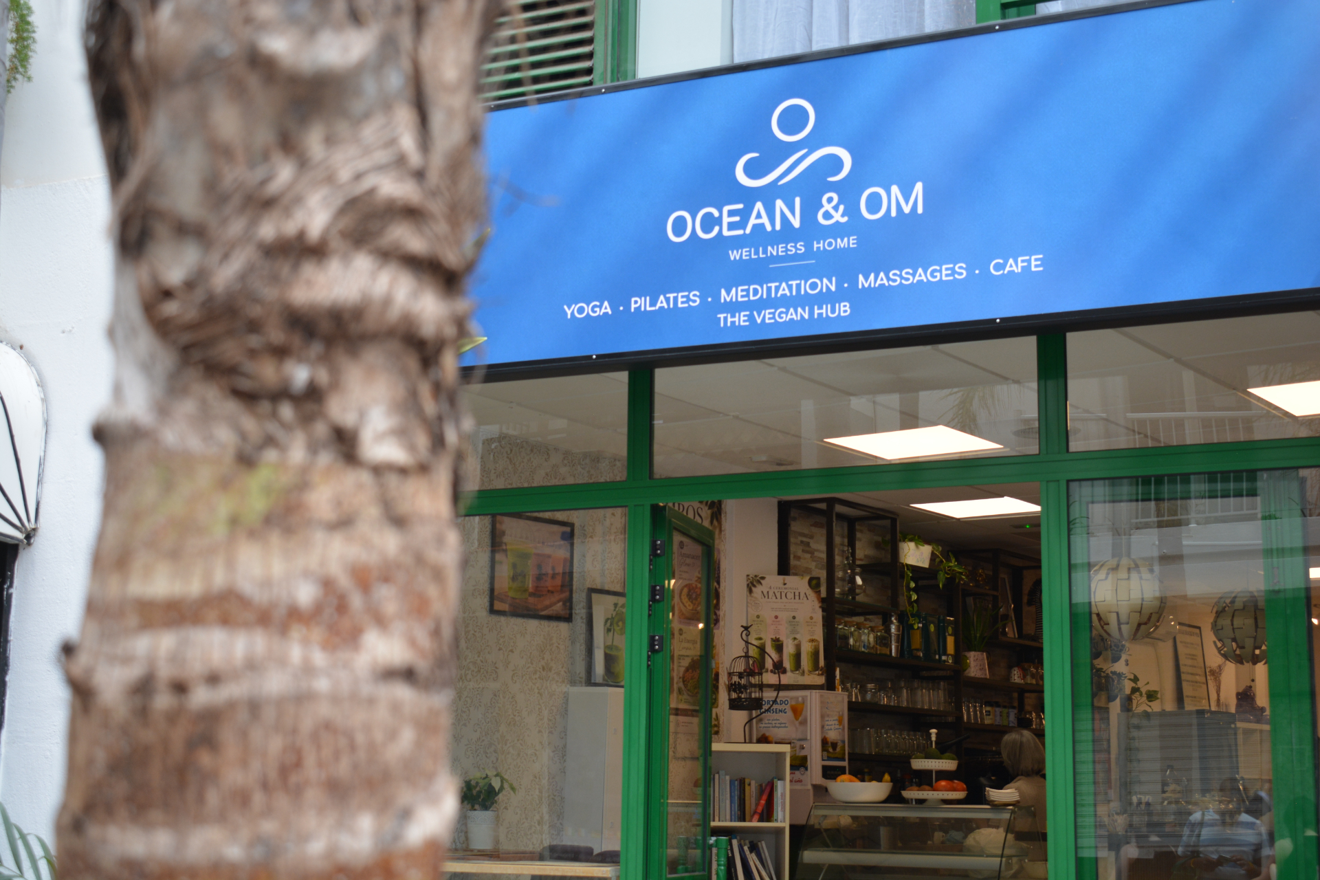 Shopfront de Ocean and Om con rotulo azul y una palmera en primer plano.