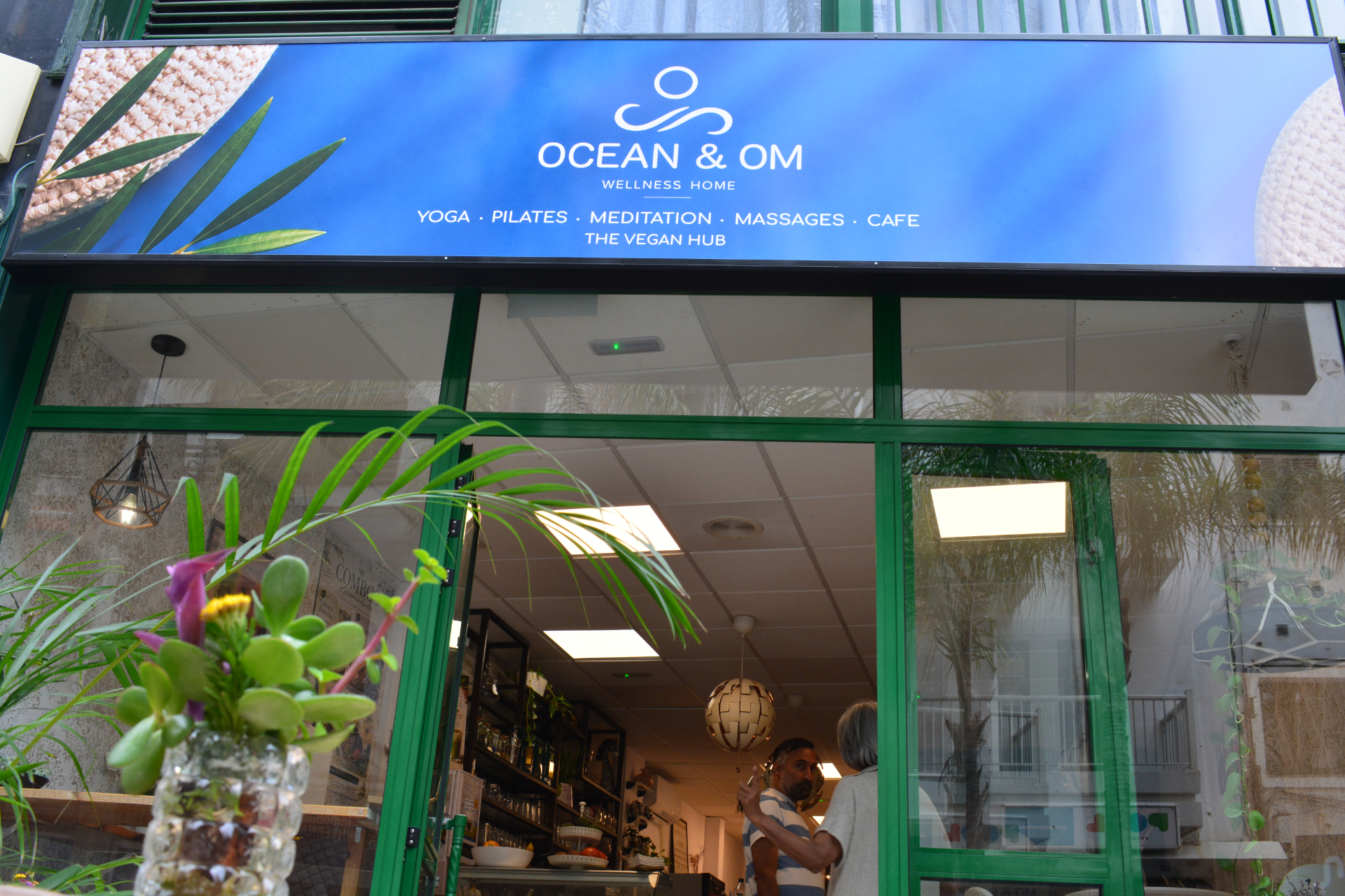 Entrada de Ocean and Om Wellness Home con rotulo azul y plantas.