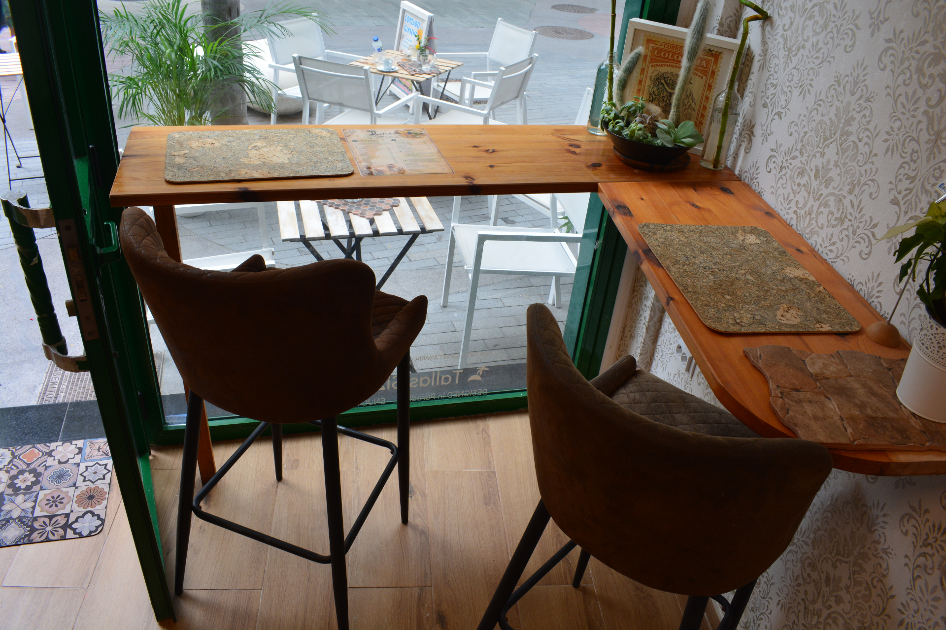 Dos taburetes junto a una barra de madera y ventana del cafe.