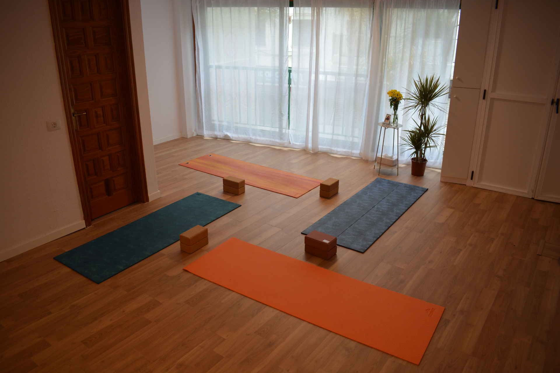 Esterillas de yoga con bloques cerca de cortinas blancas y flores amarillas.
