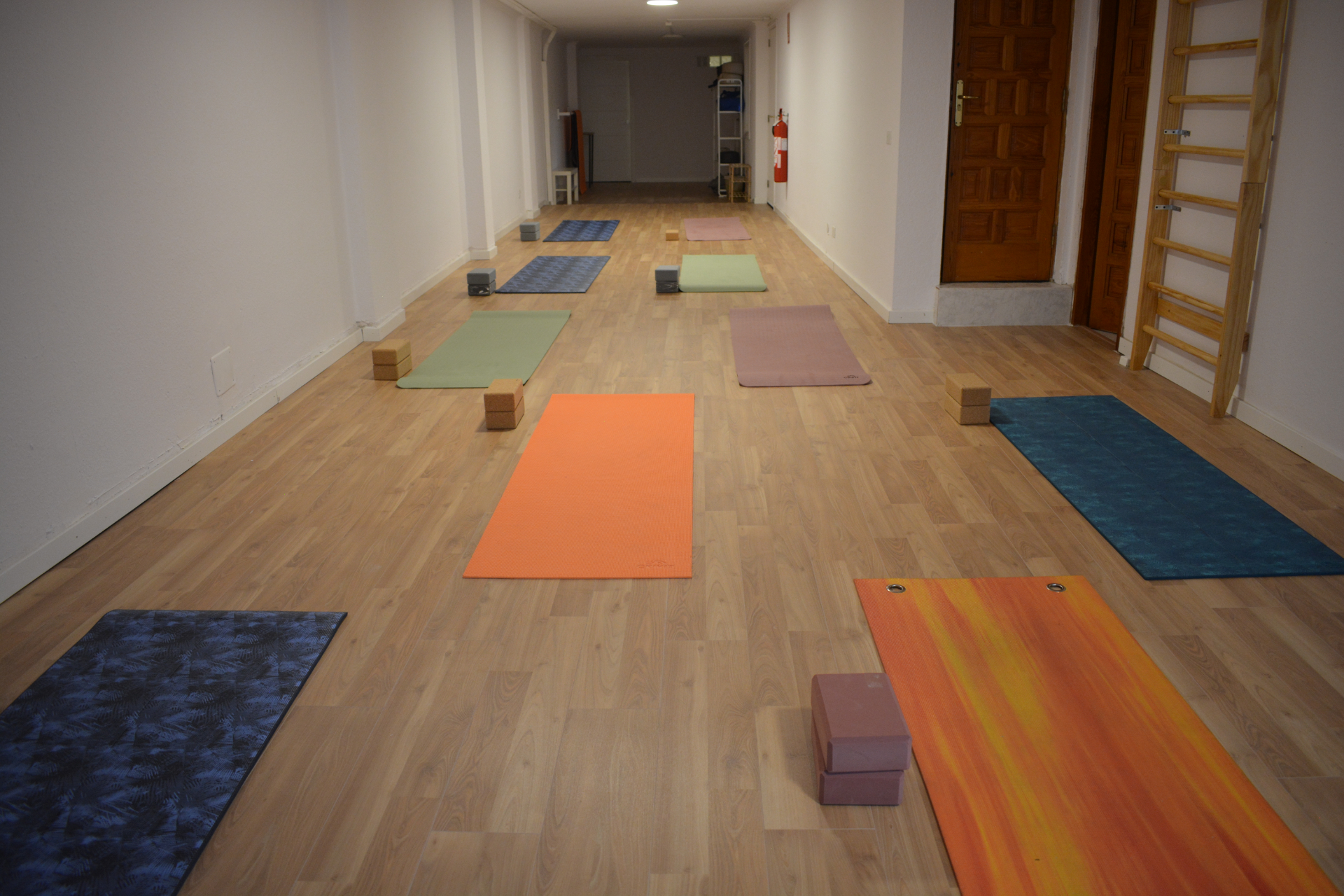 Sala de yoga con esterillas, bloques y material preparado en suelo de madera.
